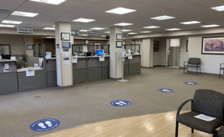 Footprint decals on the floor of a clinic indicate where people should stand at a distance from others when taking care of health care needs