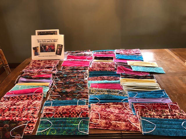 Colorful handmade face masks lined up on a wooden table with a sign about the cloth coming from Brenda Russ' collection.