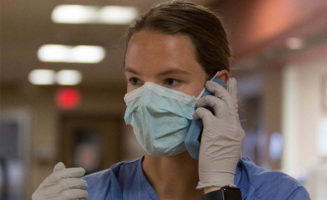 A nurse talks on a phone while wearing a mask and gloves