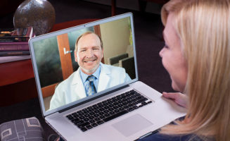 A woman smiles at a doctor on her laptop screen while he smiles back
