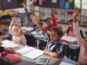 Schoolkids raising their hands in classroom.