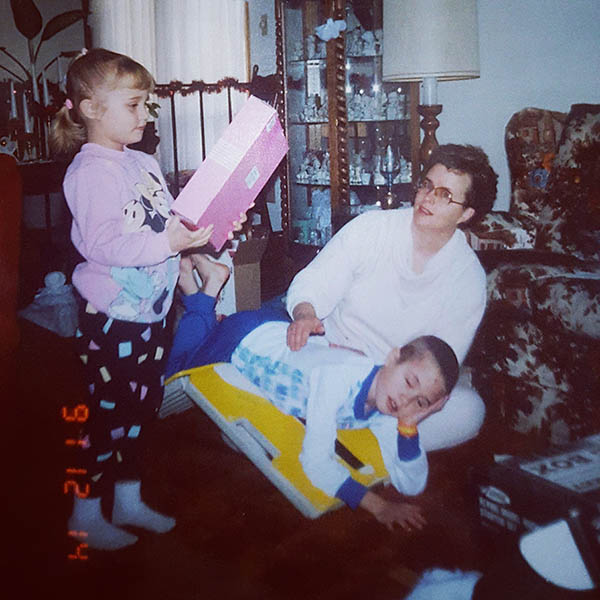 A girl holds a packaged toy while her brother lies over an angled board as his mom does chest percussion for his cystic fibrosis