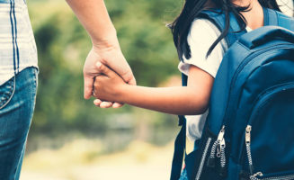 From the back, you see a mom holding the hand of her daughter, who's wearing a backpack and heading back to school
