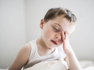 A boy rubs his eyes in bed.