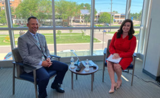 Dr. Joshua Crabtree and Courtney Collen smile in front of a wall of windows