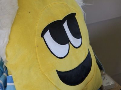 Yellow fuzzy pillow with smiling face showing emotion of happiness.
