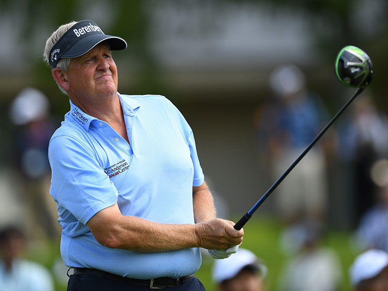Colin Montgomerie holds a golf club with spectators blurred in the background.