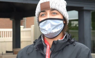 Sanford worker in stocking cap, coat and Sanford International face mask stands outside a pavilion at the golf course.