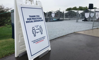 A white sandwich board sign says "Thank you for practicing social distancing. Please help us be mindful and maintain at least 6 feet distance." A graphic of two stick men with arrows adds "at least 6 ft."
