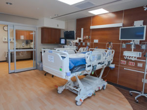 A patient bed in a private room in Sanford Heart Hospital. Warm wood tones give it a home-like feeling.