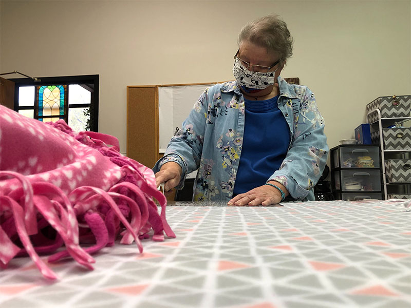 Sanford Health volunteer in face mask works on a fleece tie blanket.