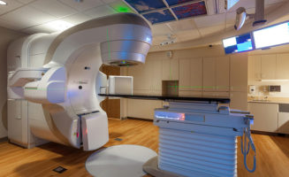 Linear accelerator marchine aims a green beam of light onto a table in a treatment room at Sanford Health.