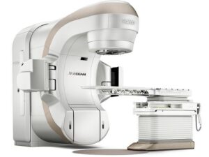 Linear accelerator machine for cancer treatment aims a beam of light onto a table on a white background.