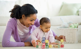 Mom and baby sit on the floor playing with wooden blocks.
