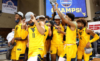 College basketball players celebrate a win at the Sanford Pentagon with a sign behind them that says CHAMPS!