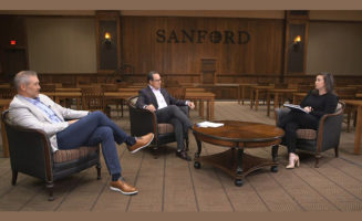 Three Sanford Health employees sit talking in a conference room, spaced 6 feet apart from each other.