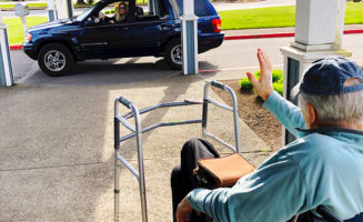 Good Samaritan Society resident in baseball cap and walker waves to young woman talking to him through her open car window.