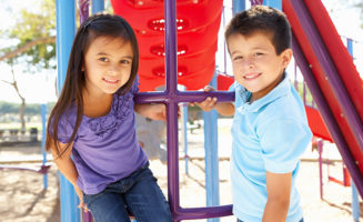 Preschool friends, a Boy And Girl On Climbing Frame In Park Smiling To Camera