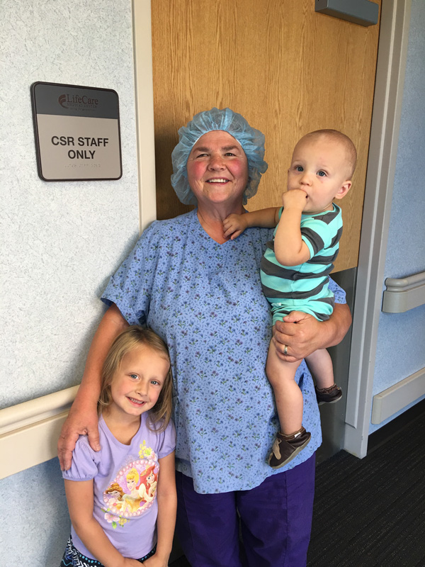 A nurse in scrubs poses in a hospital hallway with two grandchildren.