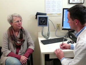 Sanford Health doctor Matthew Carpenter speaks to a senior woman patient in an exam room.