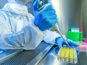 A man in full PPE injects vaccine vials under a vent hood in a lab.
