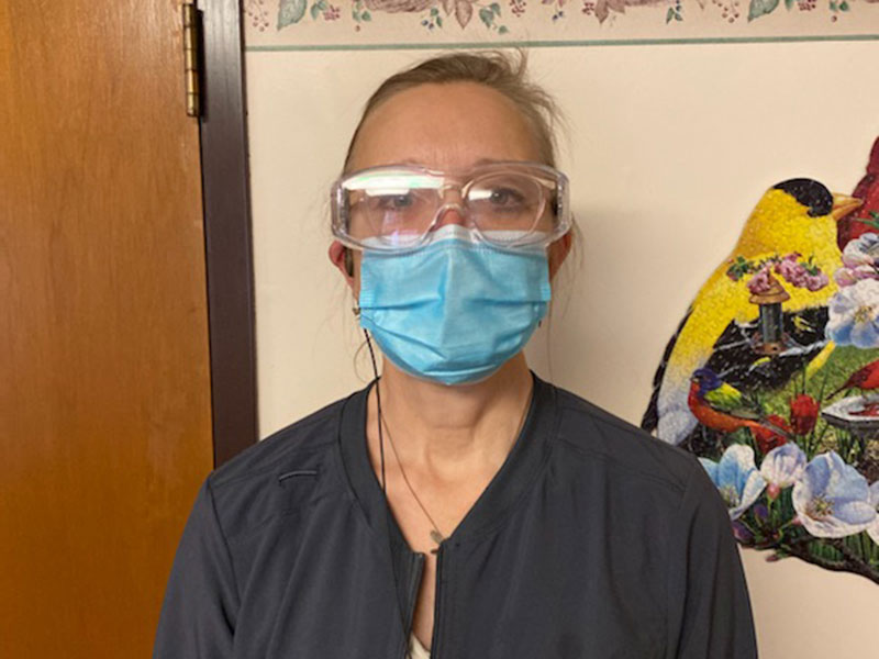 A Good Samaritan Society nurse wearing goggles and a face mask looks tired after a long shift.