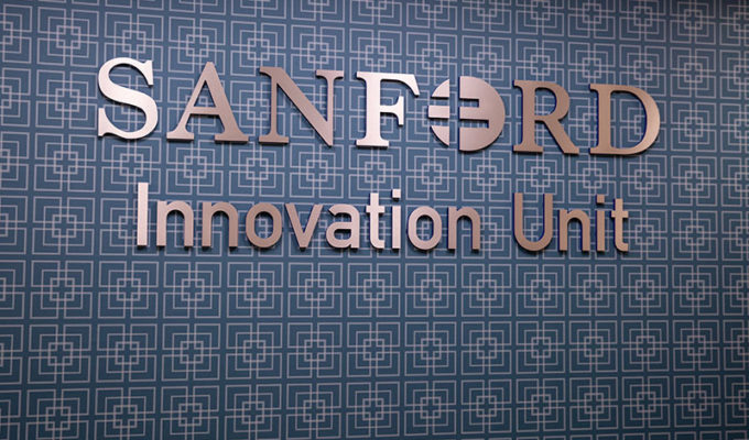 Sanford Innovation Unit sign in silver on blue patterned wall.
