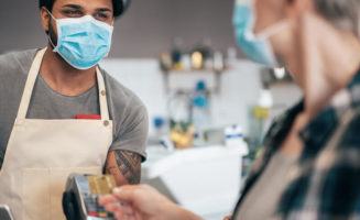 Cafe barista and mature woman are masked at the cash register