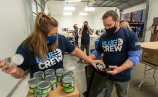 Sanford Health workers in matching "Blue Crew" T-shirts pack canned goods in a garage.