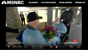 MSNBC screen shot of senior couple in protective gear and wheelchairs with headline "All in America: the year we meet again"
