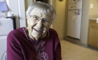 Smiling senior woman sits in her kitchen.