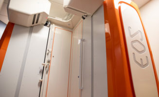 White and orange machine with "EOS" logo up the right side is ready for full-body, stand-up X-rays in an exam room.