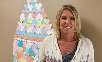 Sanford Health nurse smiles in front of a wall display of colorful paper hearts.