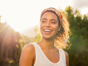 Cheerful young woman laughing at park with colorful hair band.