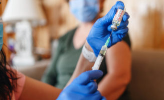 General practitioner vaccinating old patient at home with copy space. Doctor giving injection to senior woman at home. Nurse holding syringe and using cotton before make Covid-19 or coronavirus vaccine.