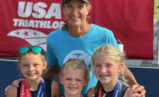 Sanford Wellness triathlon coach poses with three youth champs in front of a USA Triathlon championship banner.