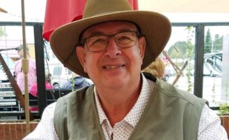 A mature male Sanford Health patient smiles at an outdoor cafe while wearing a fishing vest and hat.