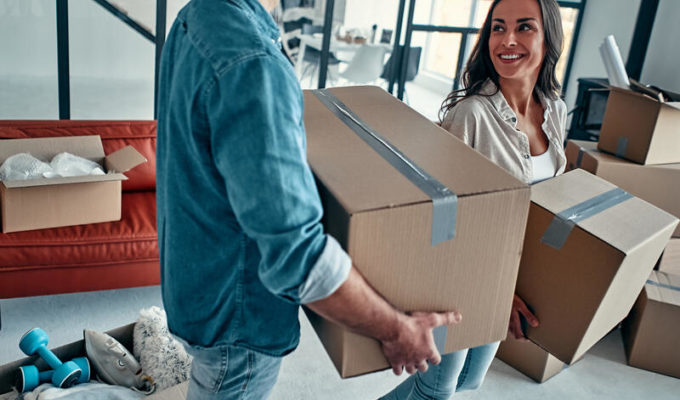 A midlife couple in the living room in the house unpack boxes with things. Happy husband and wife are having fun, are looking forward to a new home and moving with less pain.