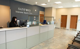 A receptionist sits behind plexiglas at the Sanford Veterans Square Clinic lobby.