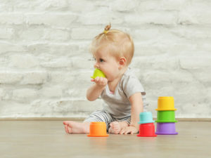 Baby girl playing on the floor with plastic educational cups.