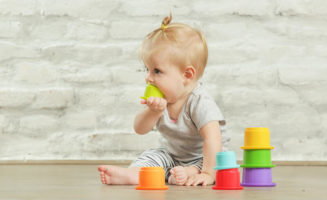 Baby girl playing on the floor with plastic educational cups.