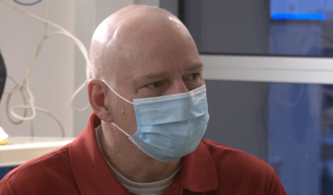 Bald man in surgical mask looks across a Sanford Health hospital exam room.