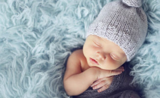 Newborn boy in grey wrap sleeping on blue blanket.