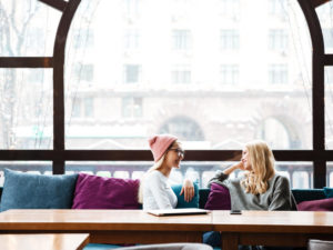 Two smiling women talking at the table in cafe.