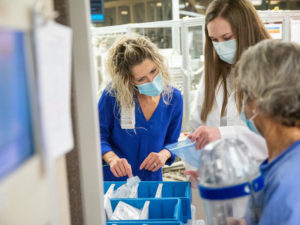 Three pharmacy workers sort bags and bins of prescription medicine at Sanford Health.