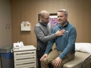 Doctor uses a stethoscope to listen to a middle-aged male patient's heart.