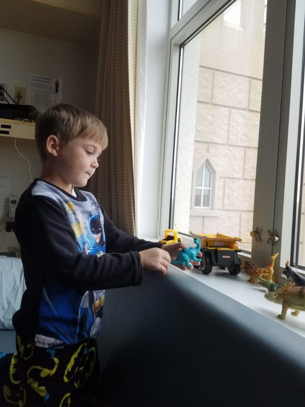 A child in pajamas plays with toy trucks and plastic dinosaurs on a windowsill at Sanford Children's Hospital.
