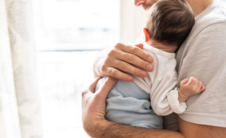 Affectionate love between father and newborn baby, father holding his son in arms in apartment.