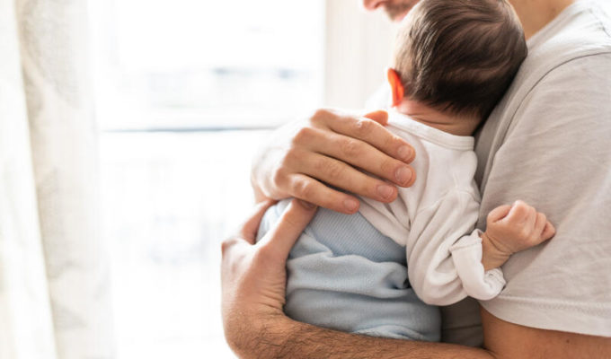 Affectionate love between father and newborn baby, father holding his son in arms in apartment.