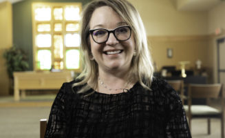 Good Samaritan Society employee smiles in sunny chapel with cross-shaped window behind her.